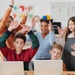 A group of happy students and a teacher clapping together in a school classroom.