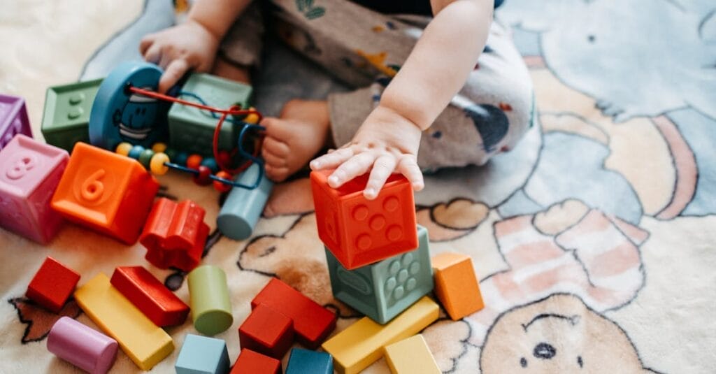 Toddler engaging with vibrant toy blocks on a patterned rug in a playful setting.