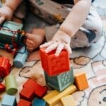 Toddler engaging with vibrant toy blocks on a patterned rug in a playful setting.