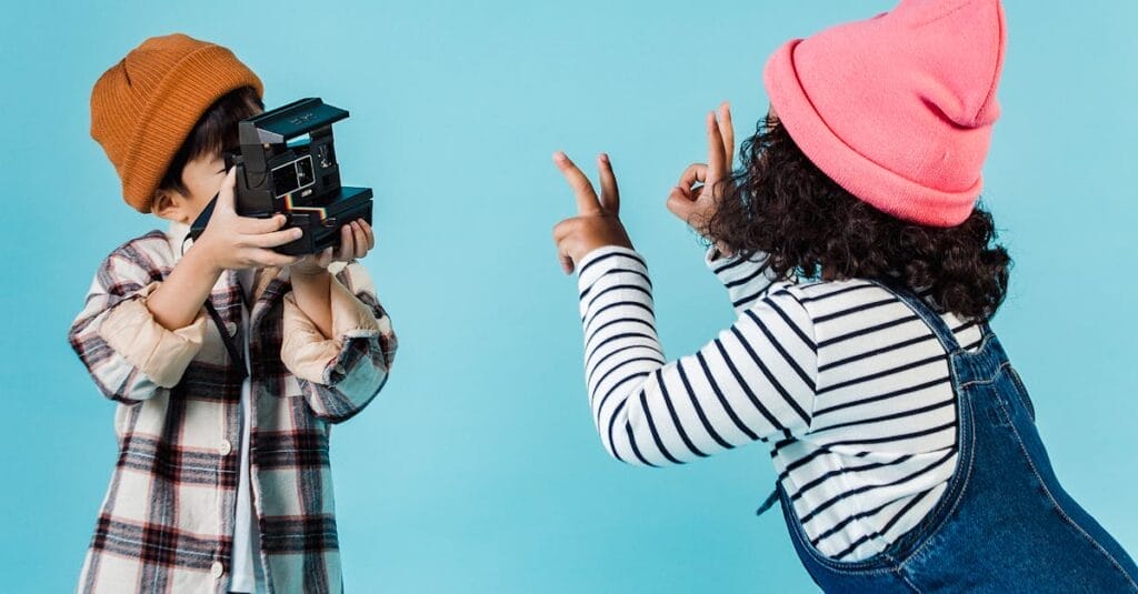 Two children in playful poses indoors capturing moments with a vintage camera.