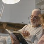 An elderly man reading a book with his granddaughter in a cozy indoor setting.