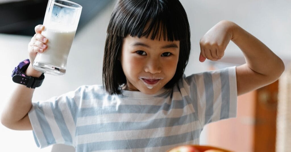 A happy child drinking milk and flexing muscles, promoting a healthy breakfast habit.