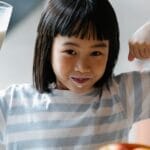 A happy child drinking milk and flexing muscles, promoting a healthy breakfast habit.