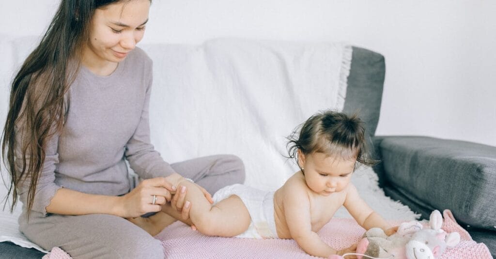 A loving mother gently massaging her baby's leg while the child plays indoors.