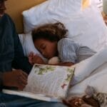 A father reads a bedtime story to his daughter, creating a calm and cozy atmosphere.