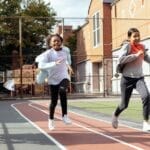 Full length of multiracial girls in sportswear and sneakers racing with each other on sports ground near school