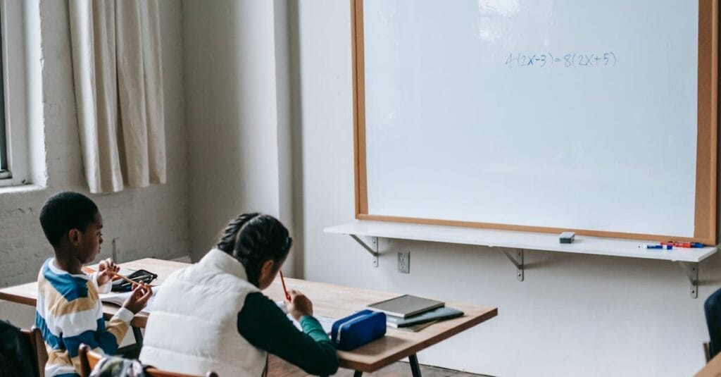 Back view African American elementary pupils in casual wear sitting at desk in light classroom and doing assignment