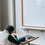 Back view African American elementary pupils in casual wear sitting at desk in light classroom and doing assignment