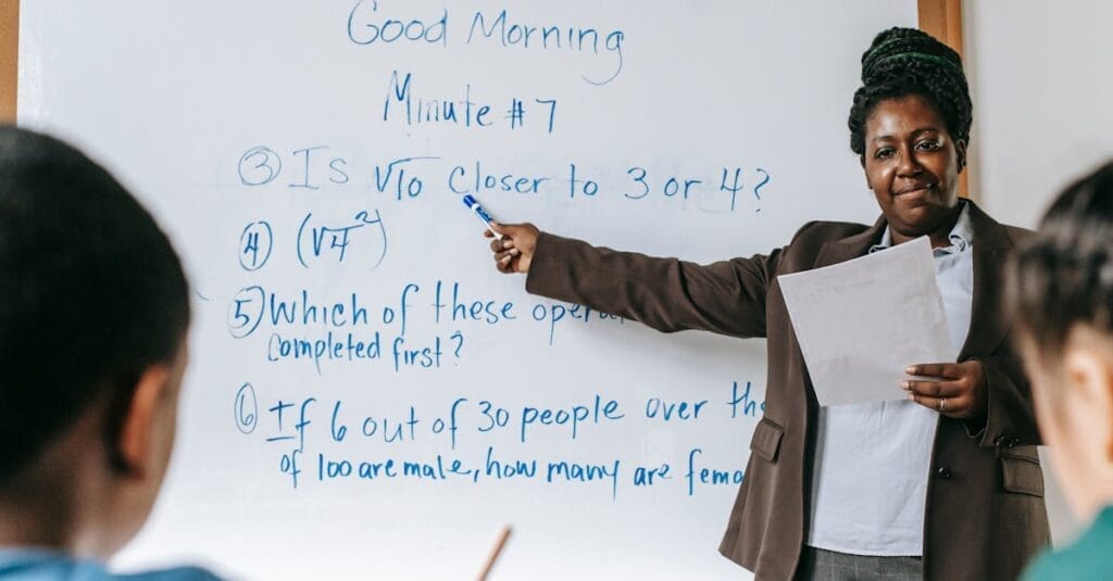 Teacher explaining math problems on whiteboard in a lively classroom setting.