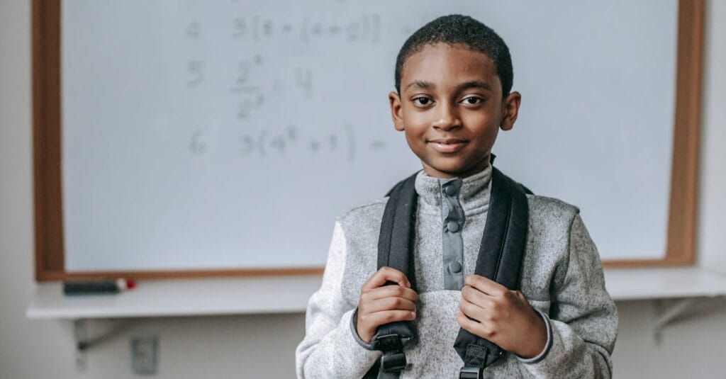 Smiling boy with backpack in classroom, ready for math class.