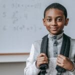 Smiling boy with backpack in classroom, ready for math class.