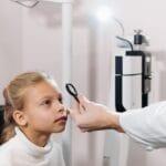 Caucasian girl undergoing an eye exam by a professional in a clinical setting.