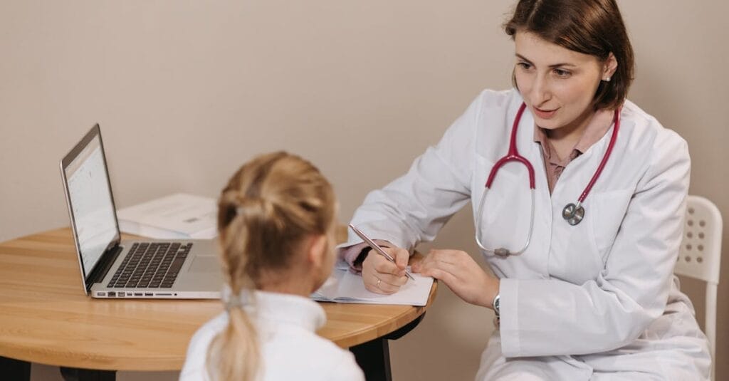 A female doctor listens attentively to a young girl during a medical consultation in an office setting.