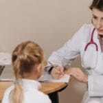 A female doctor listens attentively to a young girl during a medical consultation in an office setting.