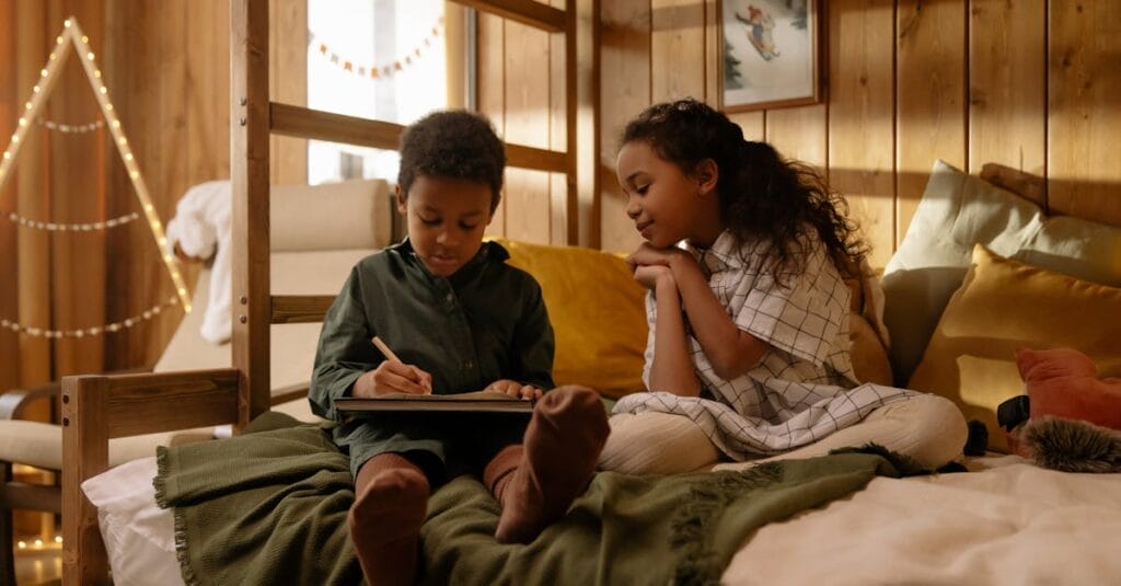 Two children sitting on a bed enjoying a book in a warmly decorated bedroom.