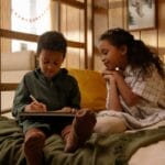 Two children sitting on a bed enjoying a book in a warmly decorated bedroom.