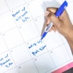 Person writing appointments on a calendar with a blue pen. High angle view.