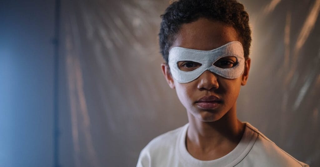 Portrait of a young child wearing a white eye mask in an indoor setting with dramatic lighting.