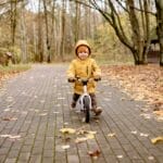 Smiling child riding a bike on a leaf-covered path in an autumn park, experiencing joy and fun.