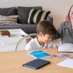 Happy grandmother assisting her grandson with homework indoors, creating a joyful learning atmosphere.