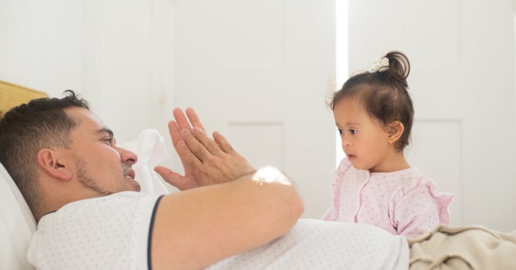 A tender moment shared between a father and his daughter in a sunlit bedroom.