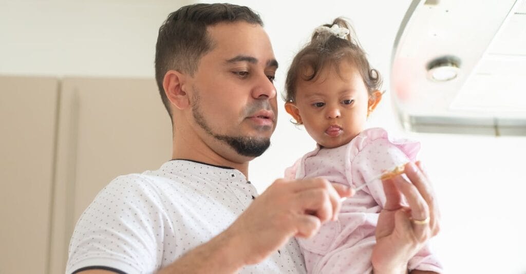 Father lovingly feeding his baby daughter in a modern kitchen.