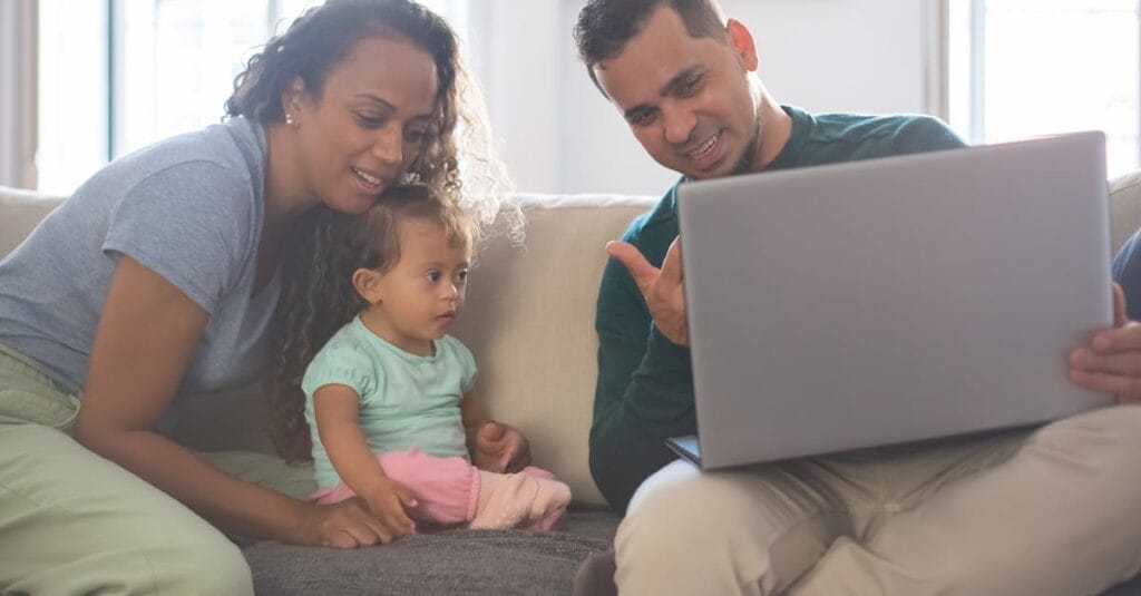 A cheerful family of three enjoying quality time together on their living room sofa, engaging with a laptop.