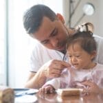 Father lovingly feeds daughter with Down syndrome during breakfast at home.