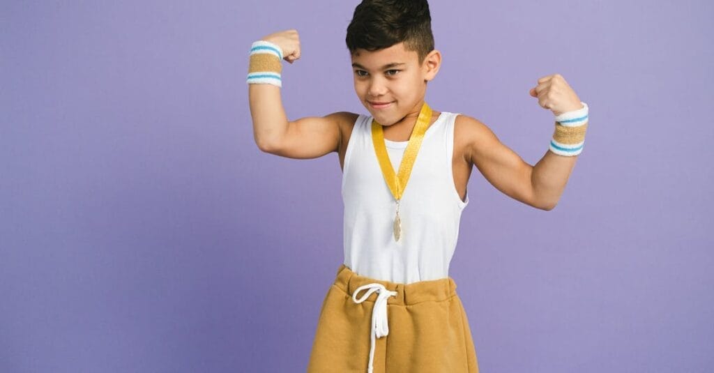 Young boy confidently flexes muscles with medal and sportswear. Perfect for themes of achievement and confidence.