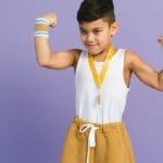 Young boy confidently flexes muscles with medal and sportswear. Perfect for themes of achievement and confidence.