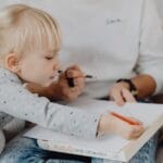 Mother and young daughter bonding over drawing activities at home, fostering creativity.