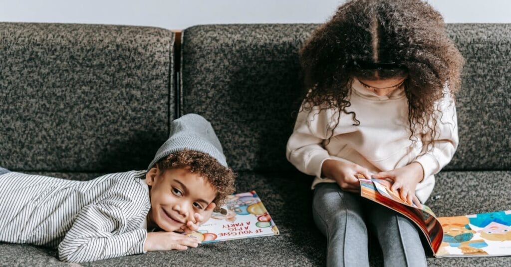 Two children enjoying books on a comfortable sofa, promoting childhood literacy and sibling bonding.