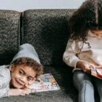 Two children enjoying books on a comfortable sofa, promoting childhood literacy and sibling bonding.