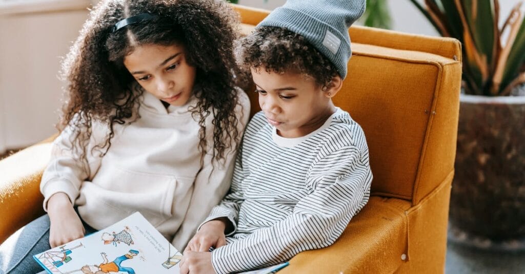 Two children reading a book on a cozy armchair, enjoying a peaceful indoor moment.