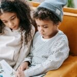 Two children reading a book on a cozy armchair, enjoying a peaceful indoor moment.