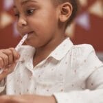 Young girl in star-patterned shirt writing indoors with a pen, reflecting thoughtfully.