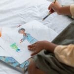 A young child creatively drawing with colored pencils at home, showcasing artistic expression.