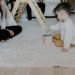 A mother and child enjoying playtime on a carpeted floor with toys.