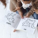 Mother and child enjoying a storytelling session with a book on a white floor.