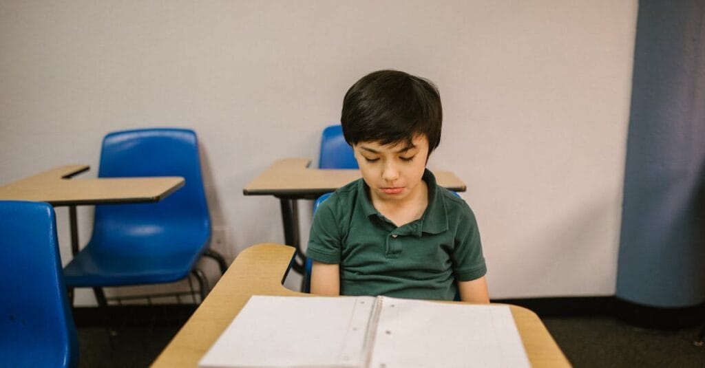 Young boy sitting alone in a classroom looking down, conveying solitude and contemplation.