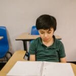 Young boy sitting alone in a classroom looking down, conveying solitude and contemplation.