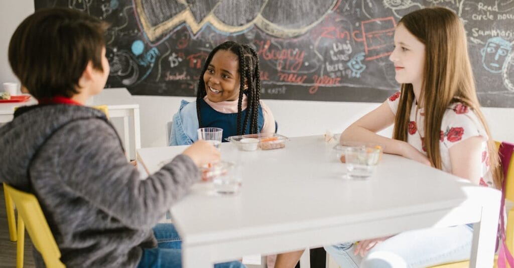 Three children engage in lively conversation during snack time at school.