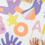 Creative art and craft layout with colorful paper cutouts and child’s hands, viewed from above.