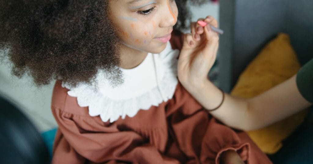 A close-up of a young girl with face paint being applied in an artistic way.