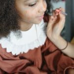 A close-up of a young girl with face paint being applied in an artistic way.