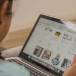 Child using laptop for online shopping, holding a credit card.