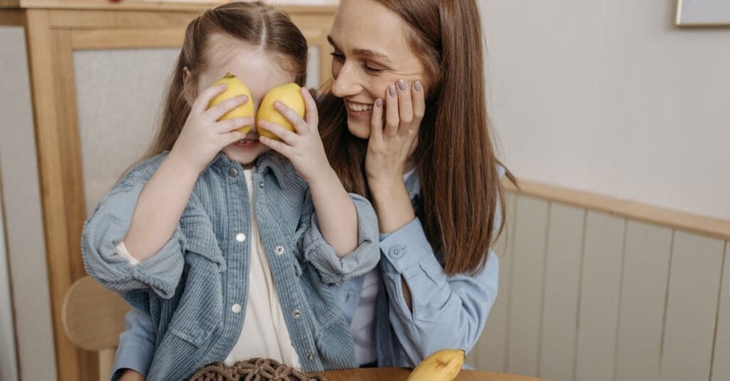 A mother and daughter share a joyful moment at home with playful lemons.