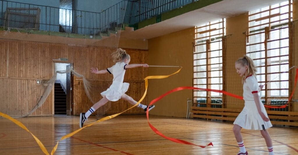 Two young girls performing rhythmic gymnastics with ribbons indoors.