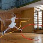 Two young girls performing rhythmic gymnastics with ribbons indoors.