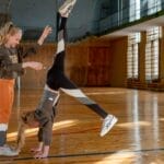 Two young girls practicing gymnastics in a sunlit gymnasium, showcasing teamwork and skill.